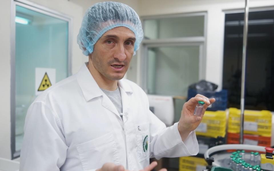 An image of a man in a lab coat and hair net holding a small bottle of antivenom.