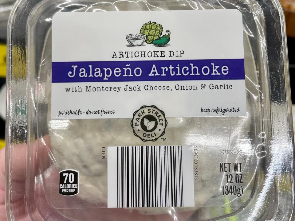 Hand holding clear package of Aldi jalepeno artichoke dip