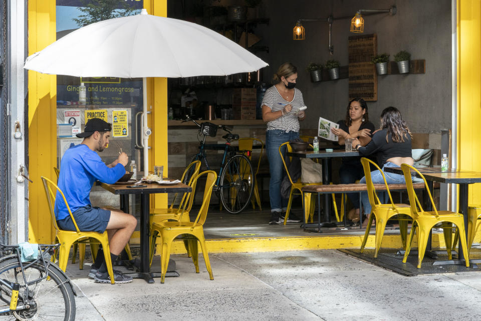 A waiter takes an order from customers sitting indoors as another has lunch at an outdoor table at Ginger and Lemongrass restaurant, Wednesday, Sept. 30, 2020, in New York. The city on Wednesday began allowing restaurants to offer indoor dining at 25 percent capacity.(AP Photo/Mary Altaffer)