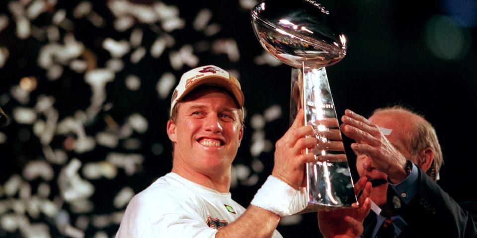 John Elway holds up the Super Bowl trophy and smiles as confetti falls at Super Bowl XXXIII.