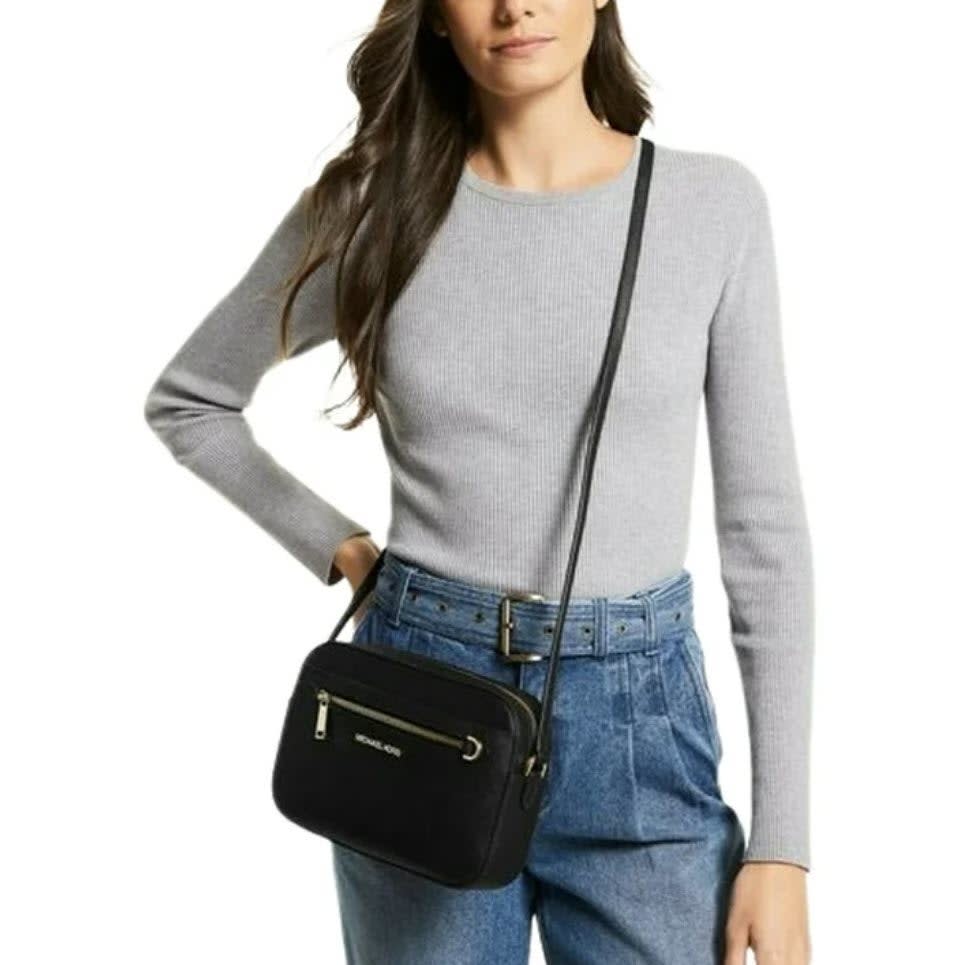 A woman is wearing a grey top and blue jeans, with a black crossbody bag