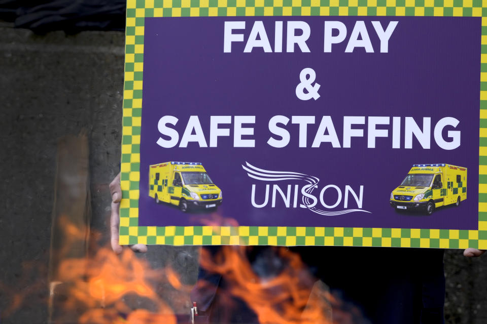 A banner is seen by a brazier as ambulance workers stand on a picket line during a strike by members of the Unison union in the long-running dispute over pay and staffing, in London, Friday, Feb. 10, 2023.(AP Photo/Kirsty Wigglesworth)