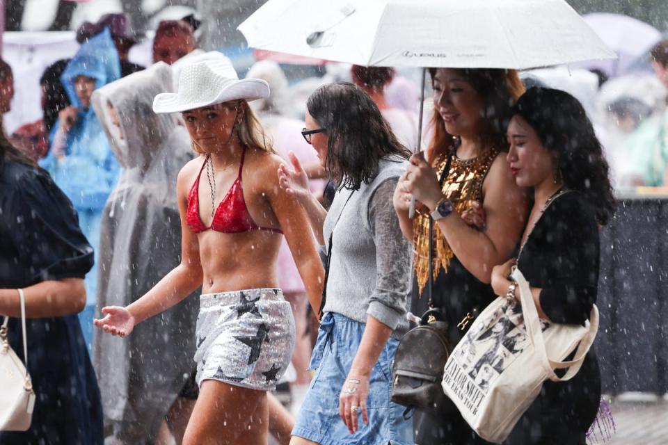 Fans of US singer Taylor Swift, also known as a Swifties, shelter from the rain as they arrive for Swift’s concert in Sydney on 23 February (AFP via Getty Images)