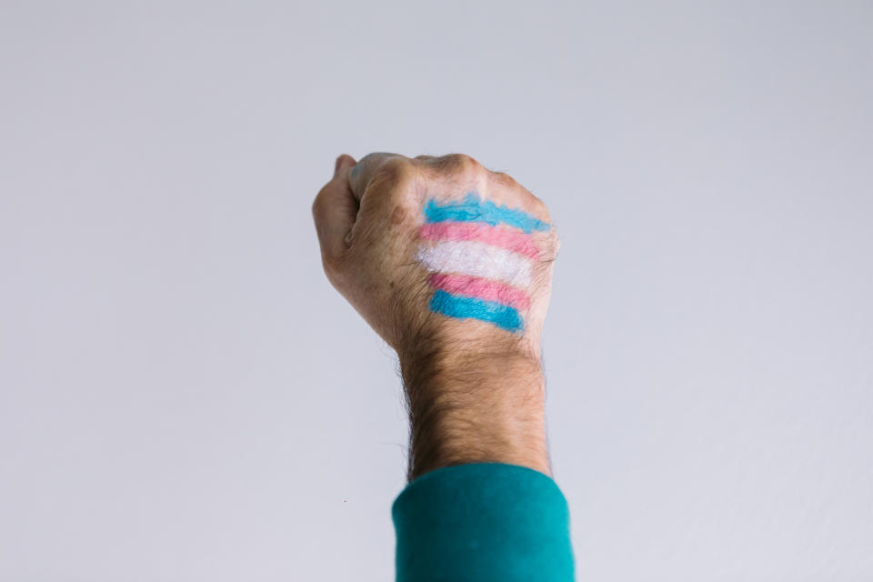 Clenched fist of a man with a painted transsexual flag, wearing an LGTBIQ flag bracelet