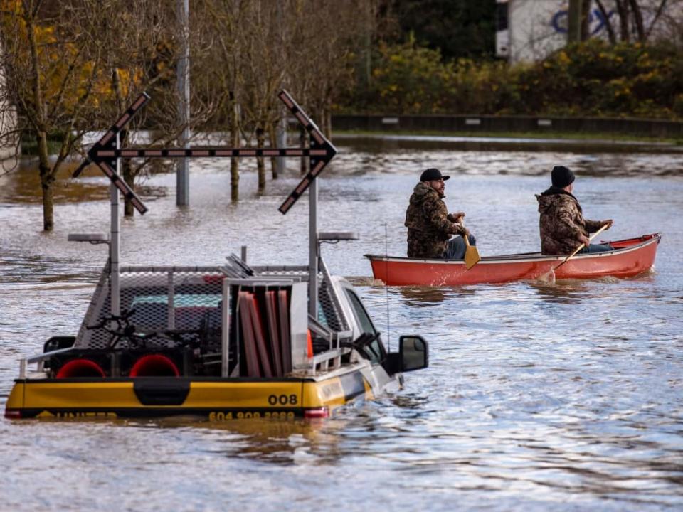 Two people canoe past a submerged truck near a flooded Trans Canada highway in Abbotsford, B.C., on Tuesday. Officials in the province were still assessing damage from floods and mudslides after torrential rains that began on the weekend finally started to subside. (Ben Nelms/CBC - image credit)