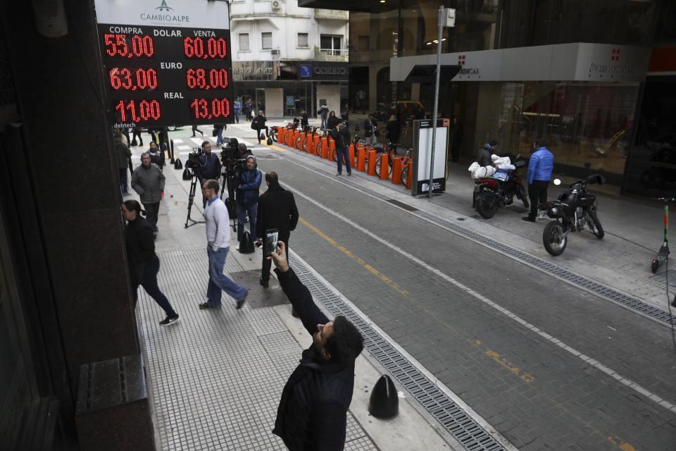 Un hombre toma una fotografía del tipo de cambio que se muestra en una pizarra de una casa de cambio en Buenos Aires, Argentina, el lunes 12 de agosto de 2019. El peso se devaluó fuertemente el lunes después de una sorprendente victoria de la oposición en las primarias presidenciales del domingo. (AP Foto / Natacha Pisarenko)