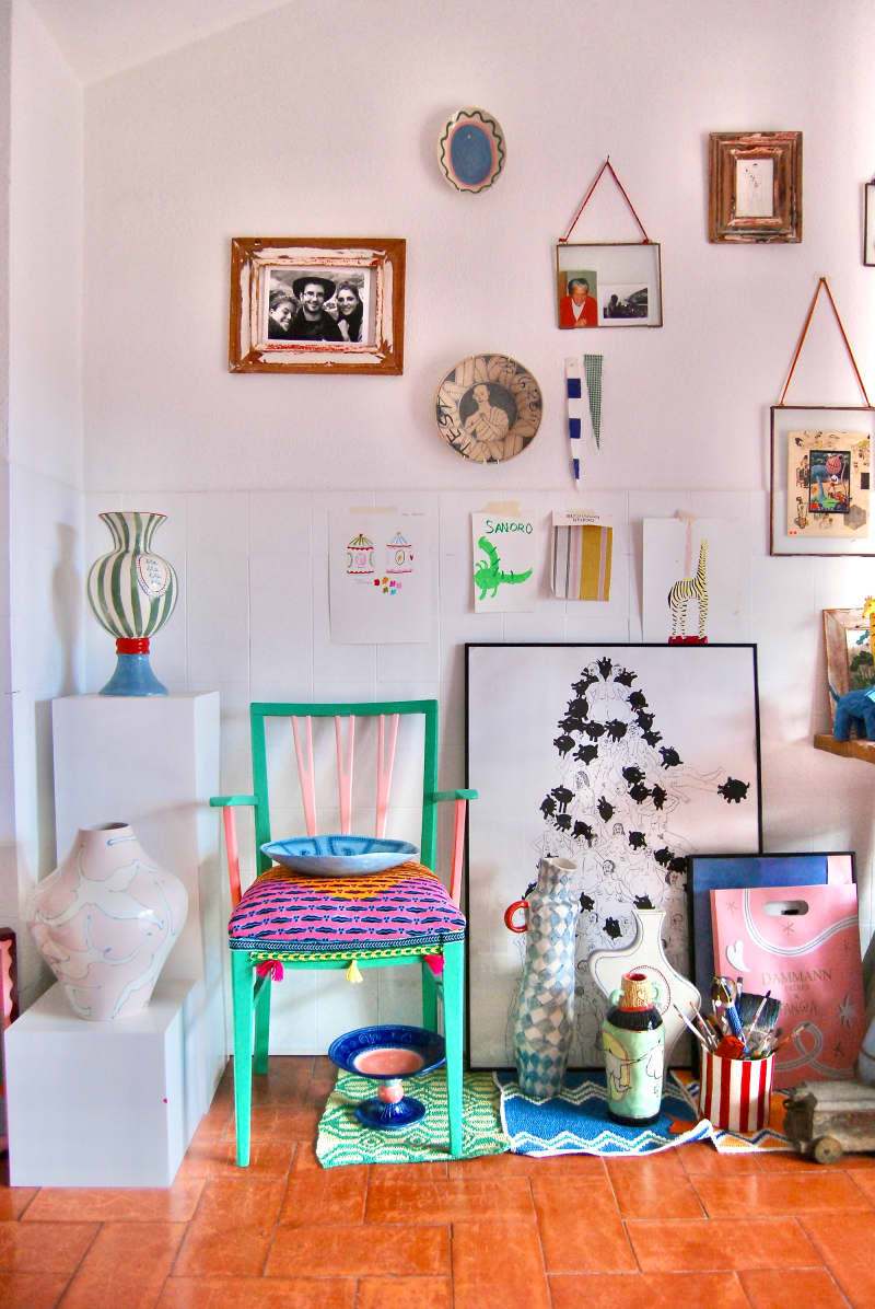 Green chair surrounded by ceramics, artwork, and art supplies in white room with rust floor.
