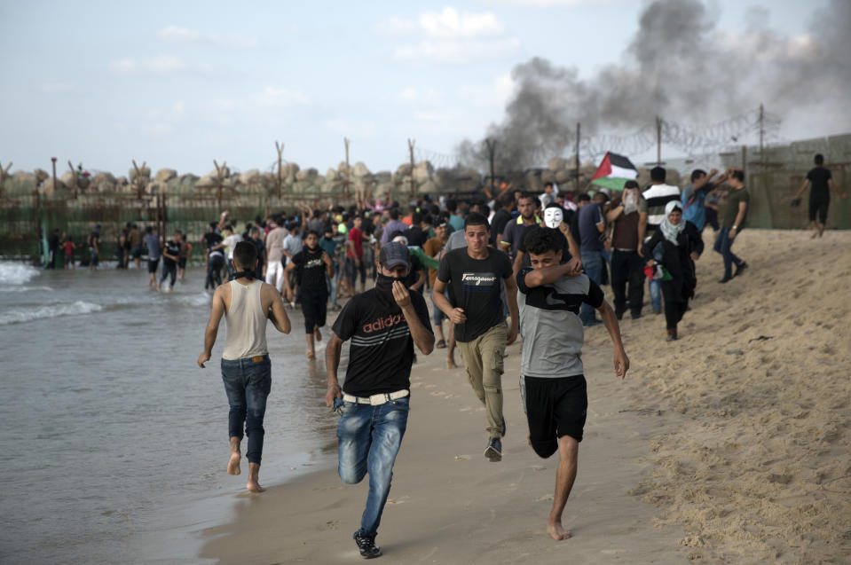 Palestinian protesters run for cover from teargas fired by Israeli troops during a protest on the beach at the border with Israel near Beit Lahiya, northern Gaza Strip, Monday, Oct. 8, 2018.(AP Photo/Khalil Hamra)