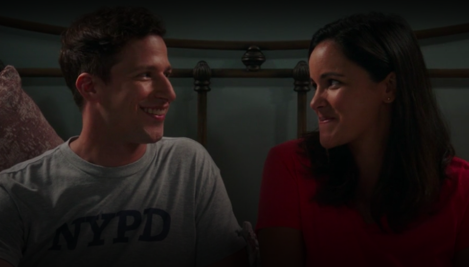 Jake and Amy smiling at each other while sitting in bed