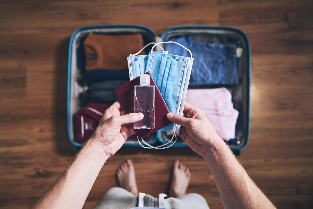 Preparing for travel in new normal. Man packing passport, face masks and hand sanitizer. Themes personal protection and flight rules during coronavirus pandemic.