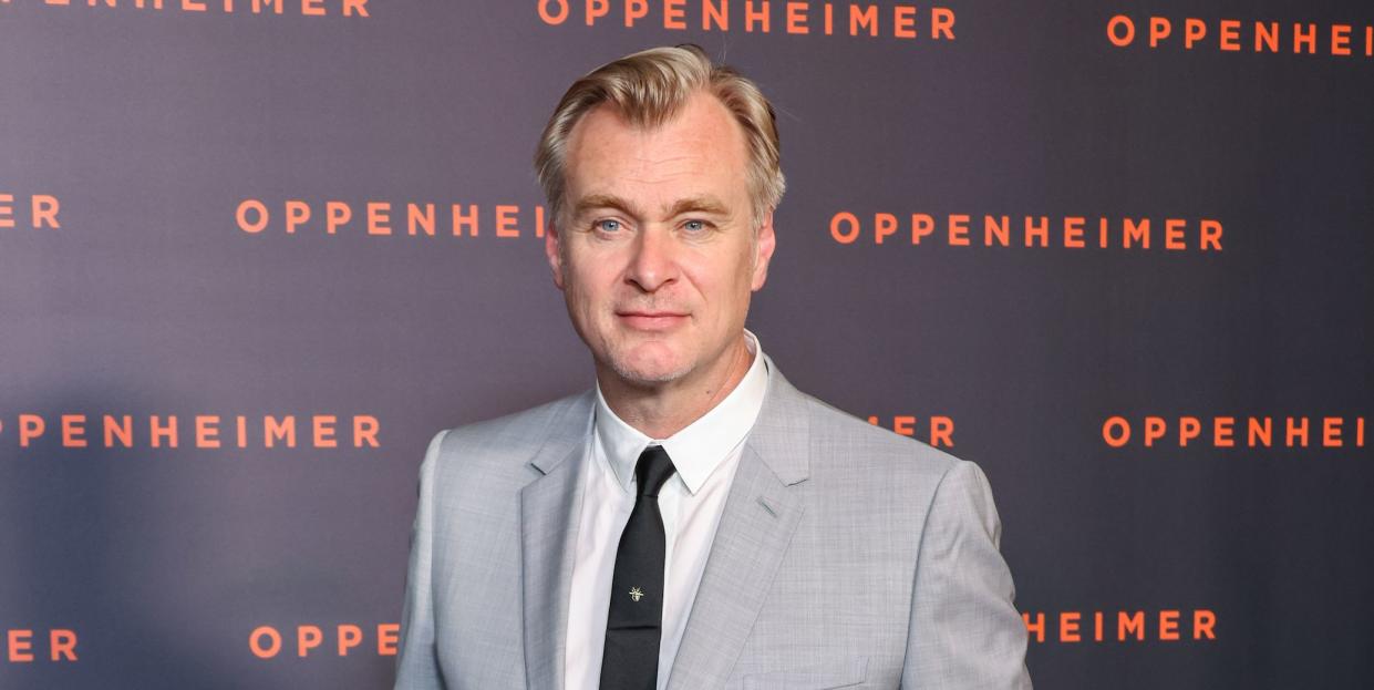 christopher nolan, a man stands with hands in trouser pockets, he wears a grey suit