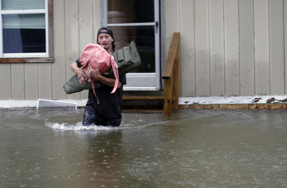 A man carries belongings from a home through thigh-high floodwaters.