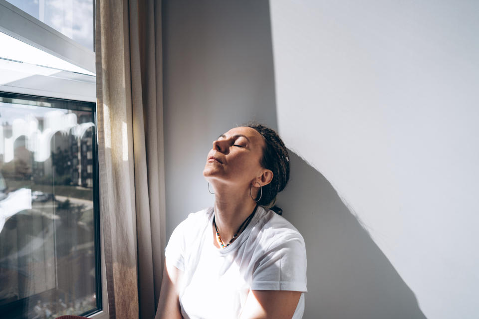 Portrait of a dreadlock braid woman sitting by the open window at the white wall. Concept of depression, loneliness, problems. Copy space for the text