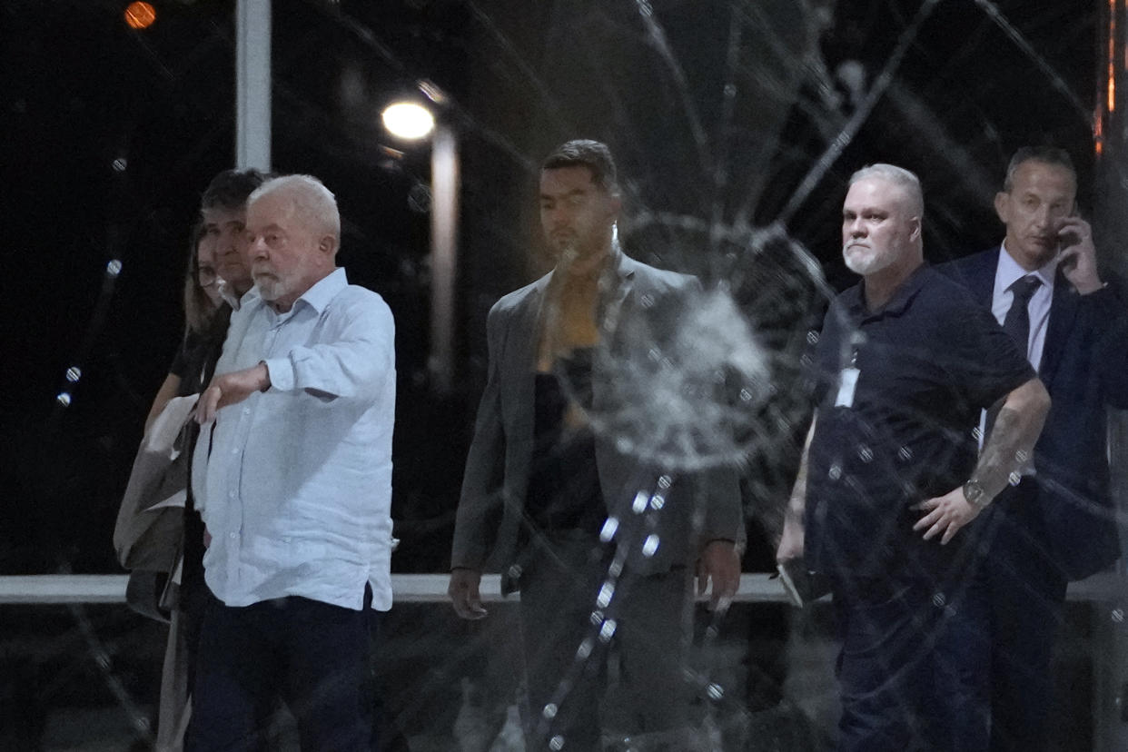 In a photo taken through a cracked window broken by a blow, President Luiz Inacio Lula da Silva and other officials inspect the damage at Planalto Palace.