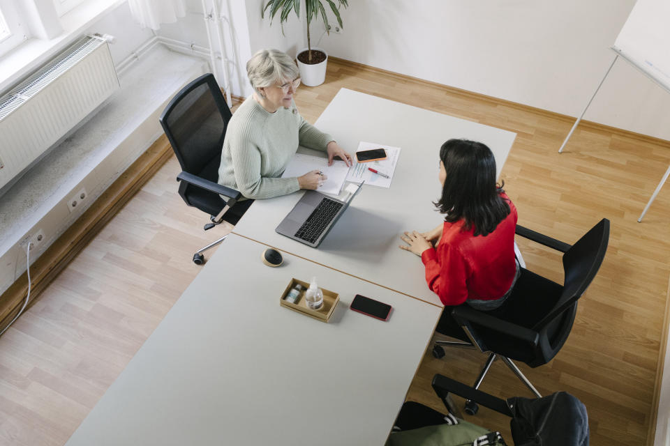 A high angle view of a businesswoman talking to one of her colleagues while siting at her desk in the office. job interviews