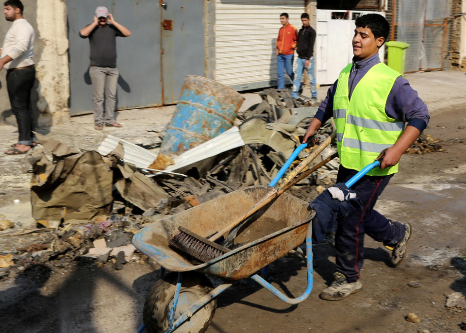 A Baghdad municipality worker cleans as civilians inspect the site of a car bomb attack near the Technology University in Sinaa Street in downtown Baghdad, Iraq, Wednesday, Jan. 15, 2014. A wave of bombings across Iraq striking busy markets and a funeral north of Baghdad killed tens of people Wednesday, authorities said, as the country remains gripped by violence after al-Qaida-linked militants took control of two cities in western Anbar province. (AP Photo/Karim Kadim)