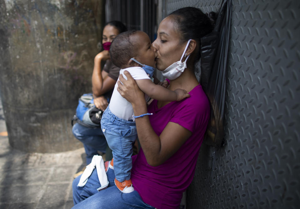 A mother kisses her baby, both equipped with protective face masks as a precaution against the spread of the new coronavirus, in Caracas, Venezuela, Thursday, May 21, 2020. (AP Photo/Ariana Cubillos)