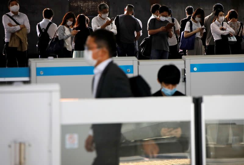 FILE PHOTO: Passengers wearing protective face masks wait for the arrival of a train amid the coronavirus disease (COVID-19) outbreak, at a train station in Tokyo