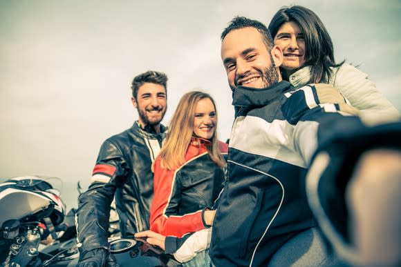 Smiling men and women by their motorcycles