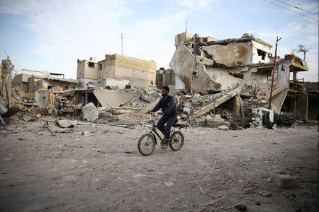 A young man rides bicycle near damaged houses in the besieged town of Douma, Eastern Ghouta, Damascus, Syria February 20, 2018. REUTERS/Bassam Khabieh