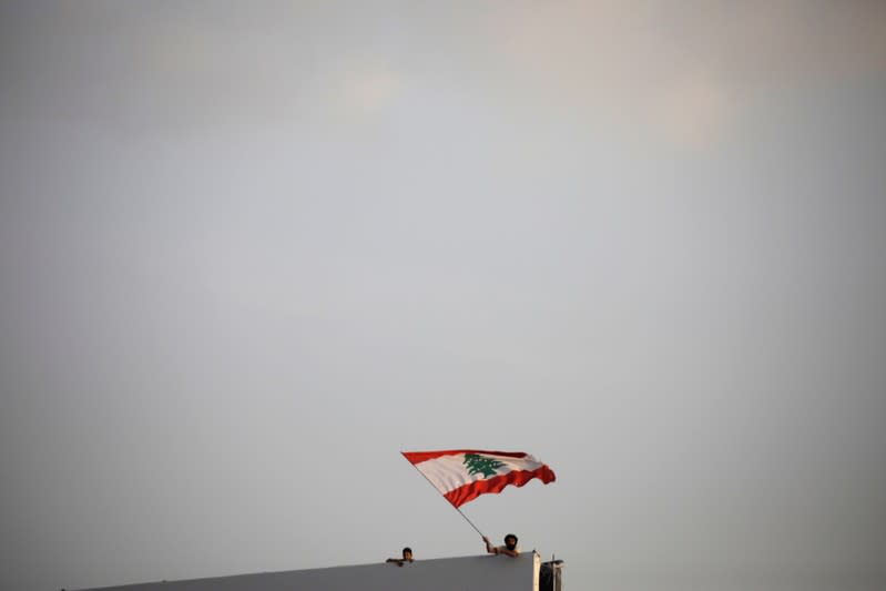 A protester waves a Lebanese flag as he stands on a billboard at a demonstration blocking the highway during ongoing anti-government protests in Hazmiyeh