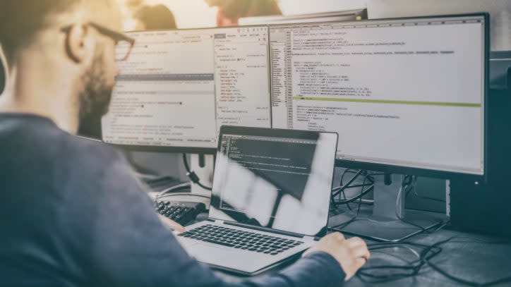 man sitting in front of 3 screens programming