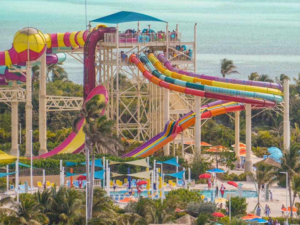 Several colorful waterslides at CocoCay with with palm trees between them and ocean waters in the background