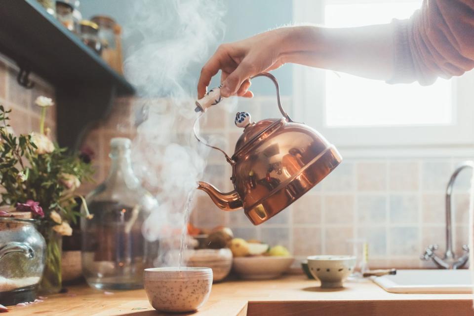 hand holding copper kettle and pouring steaming water into a bowl