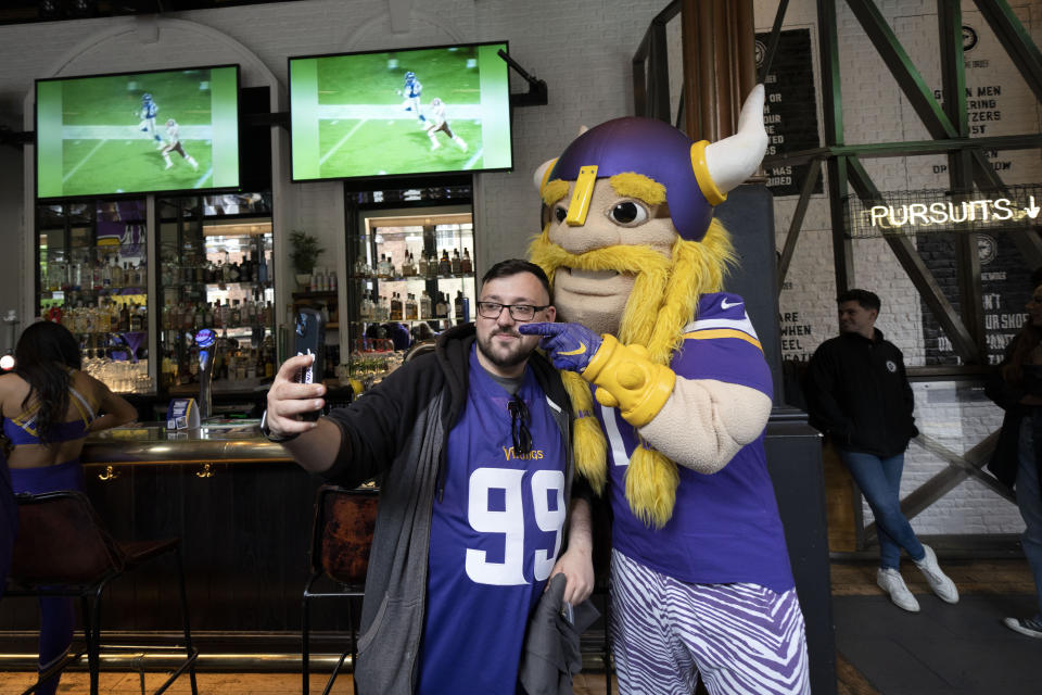 Viktor the mascot for the The Minnesota Vikings team poses for pictures with a supporter of the team at a fan interaction event at The Brotherhood Of Pursuits And Pastimes sports bar in Manchester, England, Wednesday, Sept. 28, 2022. A half-dozen NFL teams are aggressively targeting fans in Britain now that they have new marketing rights in the country. They’re signing commercial deals and hiring local media personalities in bids to expand their fanbases and tap international revenue. (AP Photo/Jon Super)