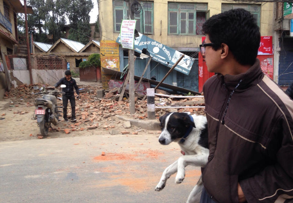 A man carries a dog and walks past damage caused by the earthquake in Kathmandu, April 25, 2015. (AP Photo/ Niranjan Shrestha)