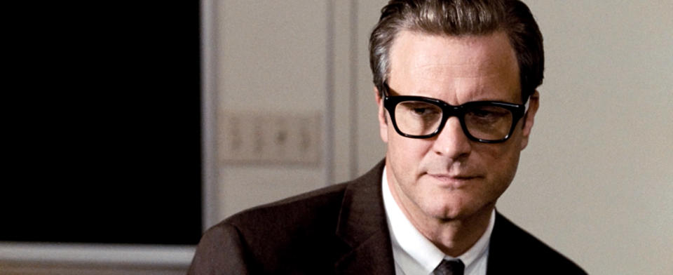 Colin Firth wearing glasses and a dark suit looks off to the side