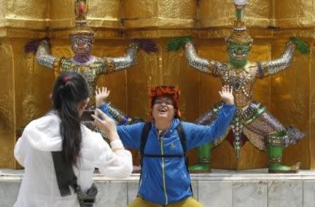 A Chinese tourist strikes a similar pose to statues as they visit the Grand Palace in Bangkok March 23, 2015. REUTERS/Chaiwat Subprasom