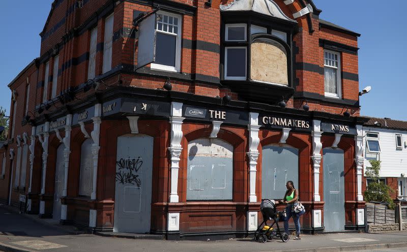 A woman pushes a pram past a closed pub in the Lozells area of Birmingham