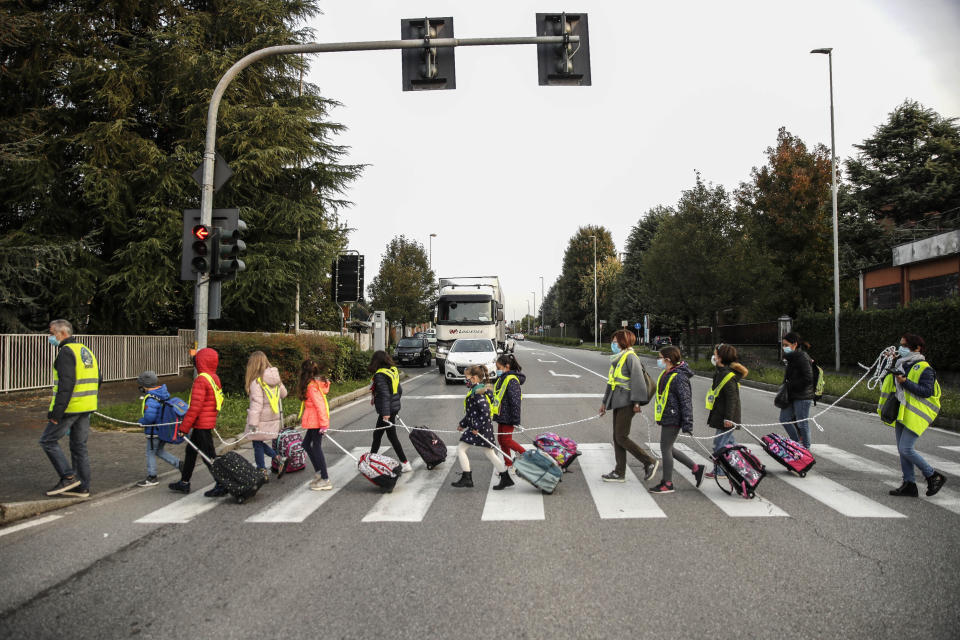 Children, escorted by volunteers, walk to school holding on to a rope to help maintain social distancing and curb the spread of COVID-19, in Bellusco, northern Italy, Tuesday, Oct. 20, 2020. (AP Photo/Luca Bruno)