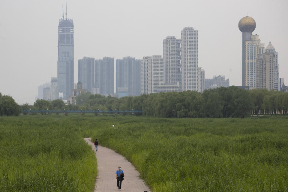 In this April 16, 2020, photo, a resident wearing a mask against the coronavirus walks through reed fields and the cityscape along the Yangtze River in Wuhan in central China's Hubei province. Wuhan has been eclipsed by Shanghai, Hong Kong and other coastal cities since the ruling Communist Party set off a trade boom by launching market-style economic reforms in 1979. But for centuries before that, the city was one of the most important centers of an inland network of river trade that dominated China's economy and politics. (AP Photo/Ng Han Guan)