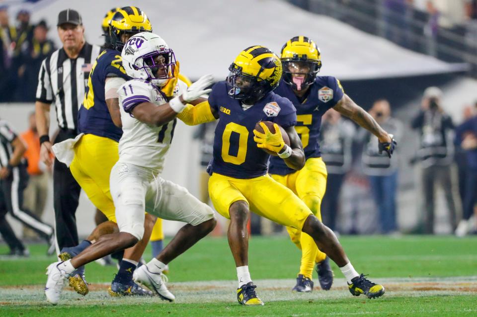 Michigan defensive back Mike Sainristil (0) runs the ball around TCU wide receiver Derius Davis (11) after interception during the third quarter in the Fiesta Bowl on Saturday, Dec. 31 at State Farm Stadium in Glendale, Ariz.