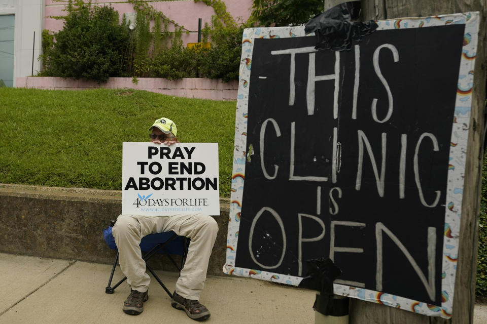FILE - An anti-abortion supporter sits behind a sign that advises the Jackson Women's Health Organization clinic is still open in Jackson, Miss., Wednesday, July 6, 2022. One year ago, the U.S. Supreme Court rescinded a five-decade-old right to abortion, prompting a seismic shift in debates about politics, values, freedom and fairness. (AP Photo/Rogelio V. Solis, File)