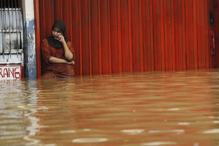 A woman stands in flood waters in front of her shop in Jakarta in this January 16, 2013 file photo. REUTERS/Enny Nuraheni/Files