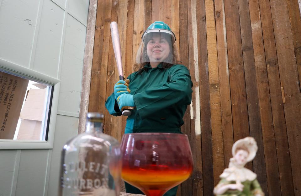 Tiffany Noell wears a jumpsuit and helmet while holding a bat at Smithereens' permanent location on Friday, Aug. 19. Patrons who come to Smithereens will be required to wear a jumpsuit and helmet for safety purposes.