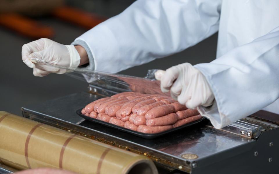 Close-up of butcher packing raw sausages at meat factory