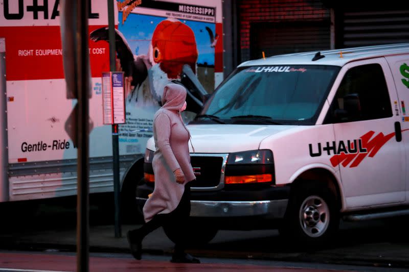 A woman walks past trucks full of bodies of deceased people outside the Andrew Cleckley Funeral Home, during the outbreak of coronavirus disease (COVID-19) in Brooklyn, New York