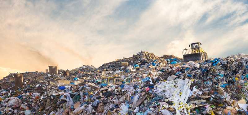 A huge mound of trash with a bulldozer perched atop it..