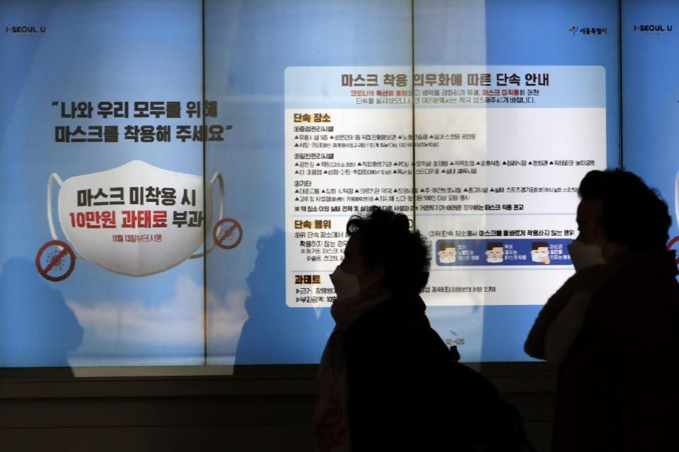 People wearing face masks walk near a screen displaying precautions against the coronavirus in Seoul, South Korea, Sunday, Dec. 27, 2020. A banner reads: "People who do not wear masks in public will face a 100,000 won (US$90) fine." (AP Photo/Lee Jin-man)