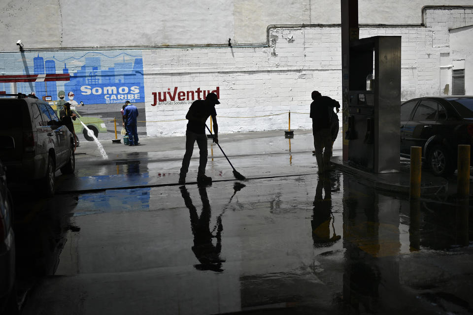 A city worker sweeps disinfectant on the ground as a preventive measure amid the spread of the new coronavirus at a state-run gas station in Caracas, Venezuela, Monday, June 29, 2020. (AP Photo/Matias Delacroix)