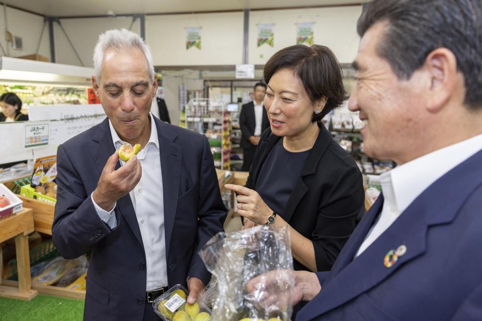 In this photo provided by U.S. Embassy, U.S. Ambassador to Japan Rahm Emanuel, left, eats a local fig at JA farmer’s market in Soma city, Fukushima prefecture, Thursday, Aug. 31, 2023. U.S. Ambassador Emanuel visited a northern Fukushima city Thursday and had seafood lunch with the mayor, talked to fishermen and stocked up on local produce at a grocery store to show they're all safe after the release of treated radioactive wastewater from the wrecked Fukushima Daiichi plant to the sea, backing Japan effort while criticizing China's ban on Japanese seafood as political.(U.S. Embassy via AP)