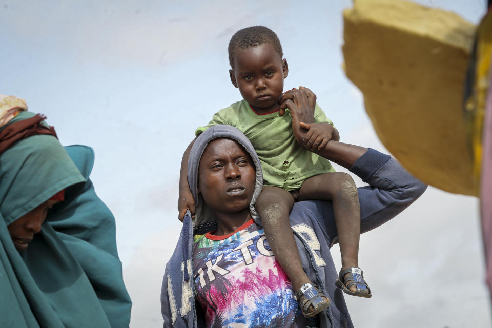 A Somali man carries a child as he and others who fled drought-stricken areas arrive at a makeshift camp for the displaced on the outskirts of Mogadishu, Somalia Thursday, June 30, 2022. The war in Ukraine has abruptly drawn millions of dollars away from longer-running humanitarian crises and Somalia is perhaps the most vulnerable as thousands die of hunger amid the driest drought in decades. (AP Photo/Farah Abdi Warsameh)