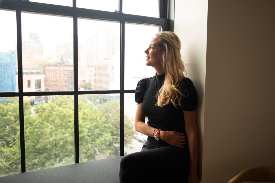 A woman sits on a wide window sill and looks out a large window.