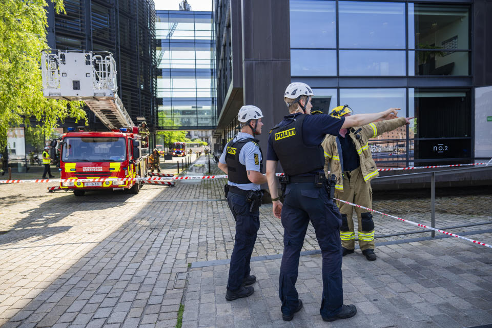 Firefighters and police officers point towards the building housing the Danish Taxation Ministry, where a fire broke out, in Copenhagen, Denmark, Thursday June 27, 2024. A fire on Thursday broken out on top of a building housing Denmark’s Taxation Ministry in downtown Copenhagen, leading to the evacuation of the people inside the harbor-front glass-and-steel constrution and from adjacent houses. There was no word on casulaties.(Martin Sylvest/Ritzau Scanpix via AP)