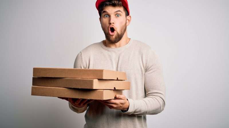 A man holds a stack of pizza boxes against a gray background