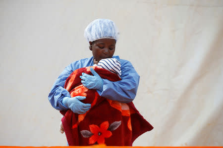 Rachel Kahindo, an Ebola survivor working as a caregiver to babies who are confirmed Ebola cases, holds an infant outside the red zone at the Ebola treatment centre in Butembo, Democratic Republic of Congo, March 25, 2019. REUTERS/Baz Ratner